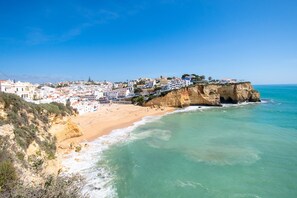 Un pueblo costero con edificios sobre un acantilado con vistas a una playa de arena y aguas turquesas.