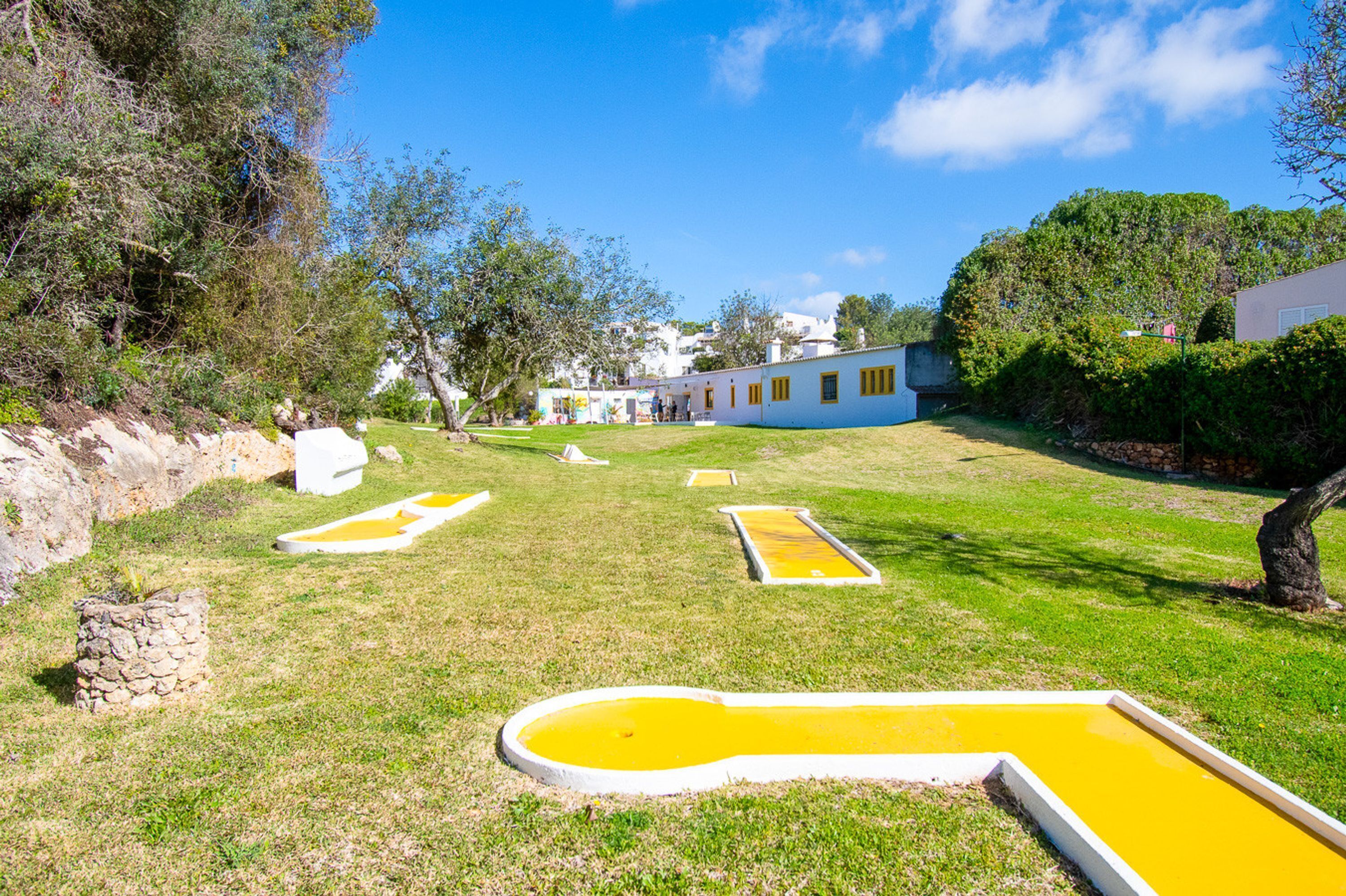 A grassy area with yellow rectangular pools and a white building with yellow windows in the background.