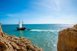 A boat sailing on a clear blue sea with rocky cliffs in the foreground. - C65 Quinta do Paraiso (Lagoa)