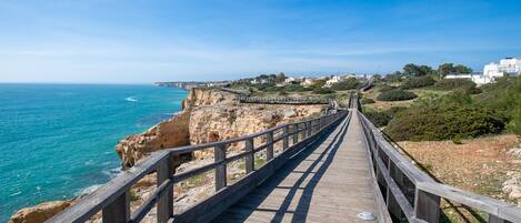 A wooden boardwalk leading to a coastal area with rocky cliffs and a clear blue sky.