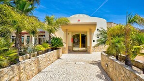 A building with a curved facade, a stone pathway leading to the entrance, and tropical plants surrounding the area. - 7 Boa Nova Immaculately Presented TWO Storey TOW (Lagoa)