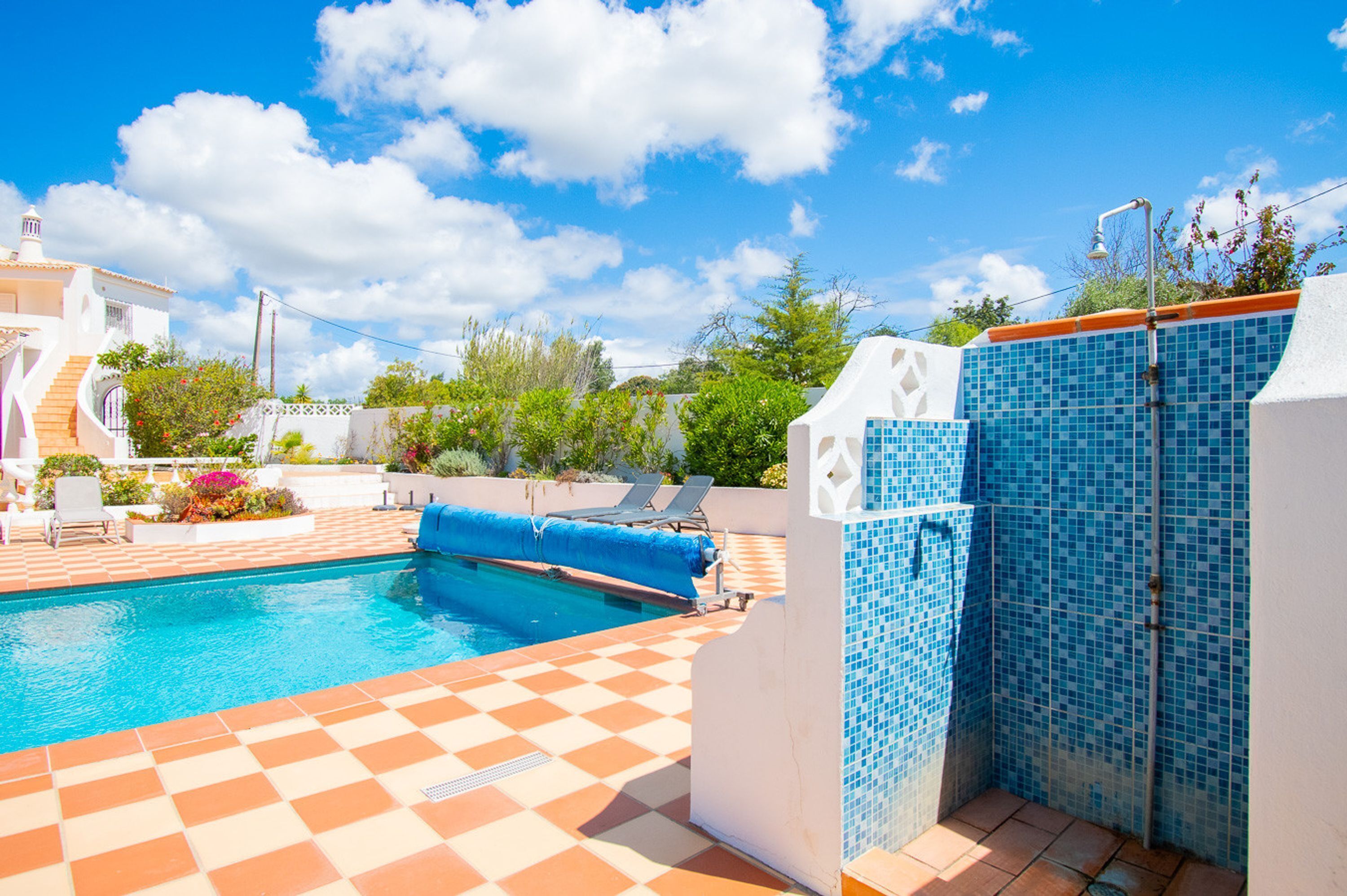 A swimming pool with a checkered floor, lounge chairs, and a tiled wall.