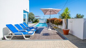 Un área junto a la piscina con sillas reclinables azules, piscina y sombrillas.