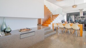 Cocina moderna con una isla central, escalera de madera y zona de comedor con sillas.