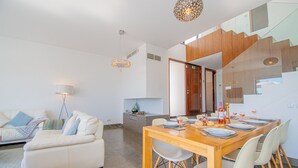 Una sala de estar moderna con un sofá blanco, una mesa de comedor preparada para cuatro personas y una escalera que sube a un nivel superior.