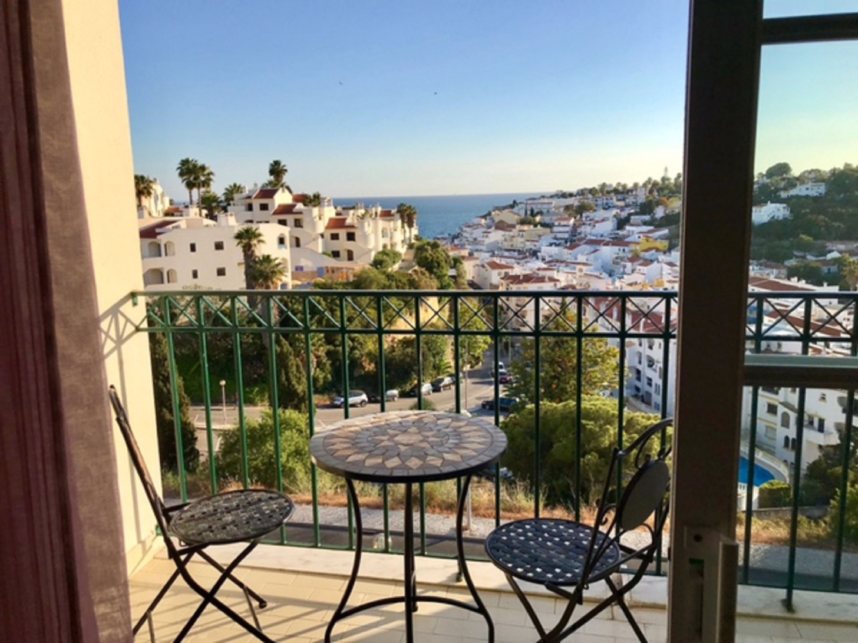 Un balcon donnant sur une ville côtière, avec une table ronde et deux chaises.
