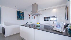 A modern kitchen with white cabinetry, a central island, stainless steel appliances, and a painting on the wall. - Casa Mar a Vista Best View in Town (Lagoa)