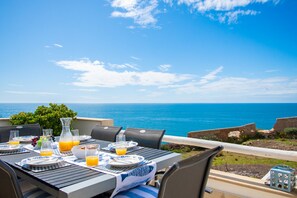 An outdoor dining table set with plates, glasses, and a pitcher of orange juice, overlooking a scenic ocean view. - Casa Mar a Vista Best View in Town (Lagoa)
