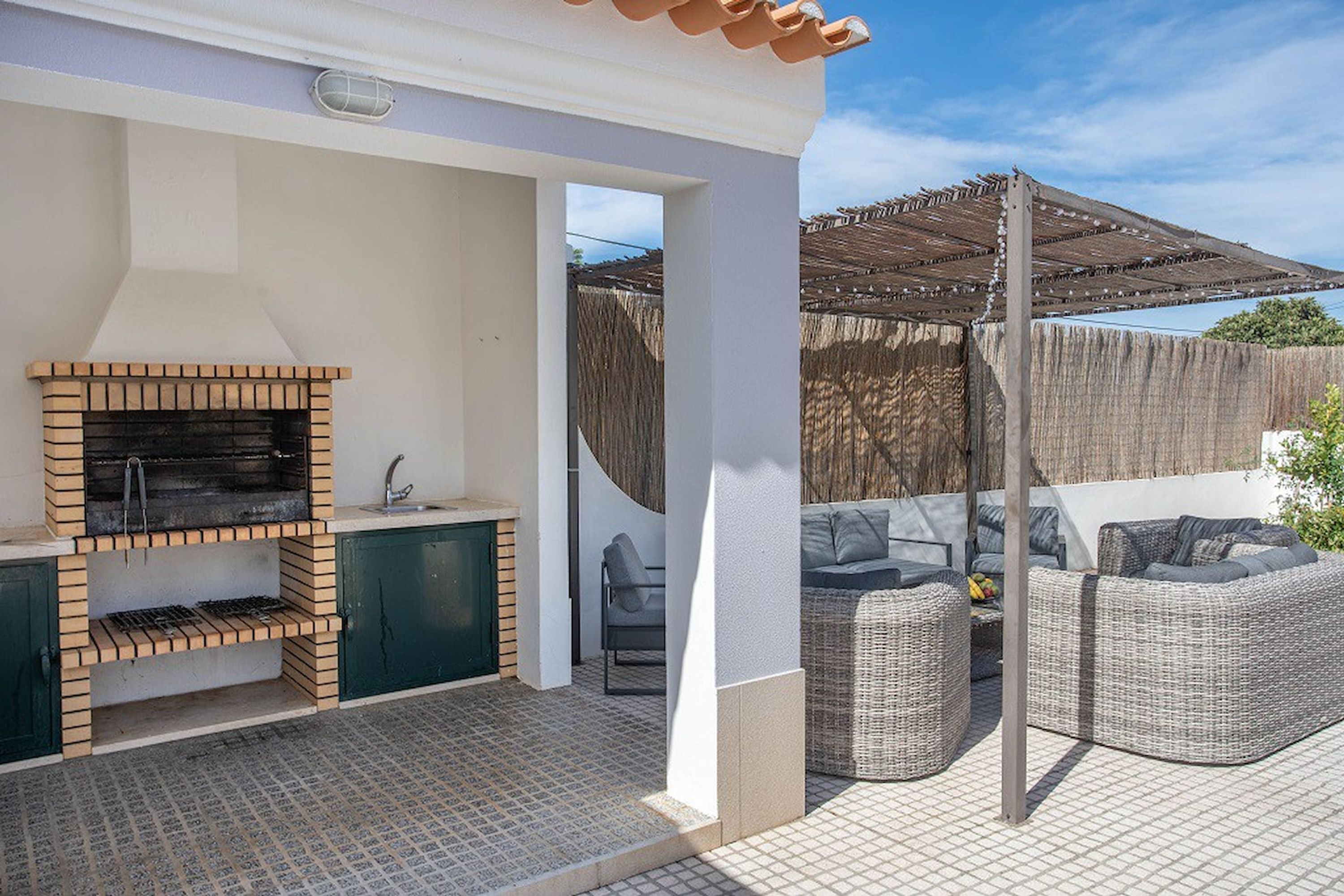 Eine Terrasse im Freien mit einem Ziegelgrill, Korbmöbeln und einem überdachten Bereich.