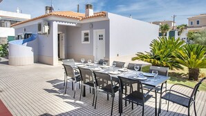 Un área de comedor al aire libre con un edificio blanco, piso de baldosas y una escalera de caracol.