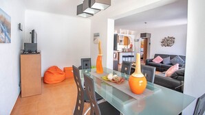 Una sala moderna con una mesa de comedor de vidrio, sillones orejeros naranjas y un sofá con cojines.
