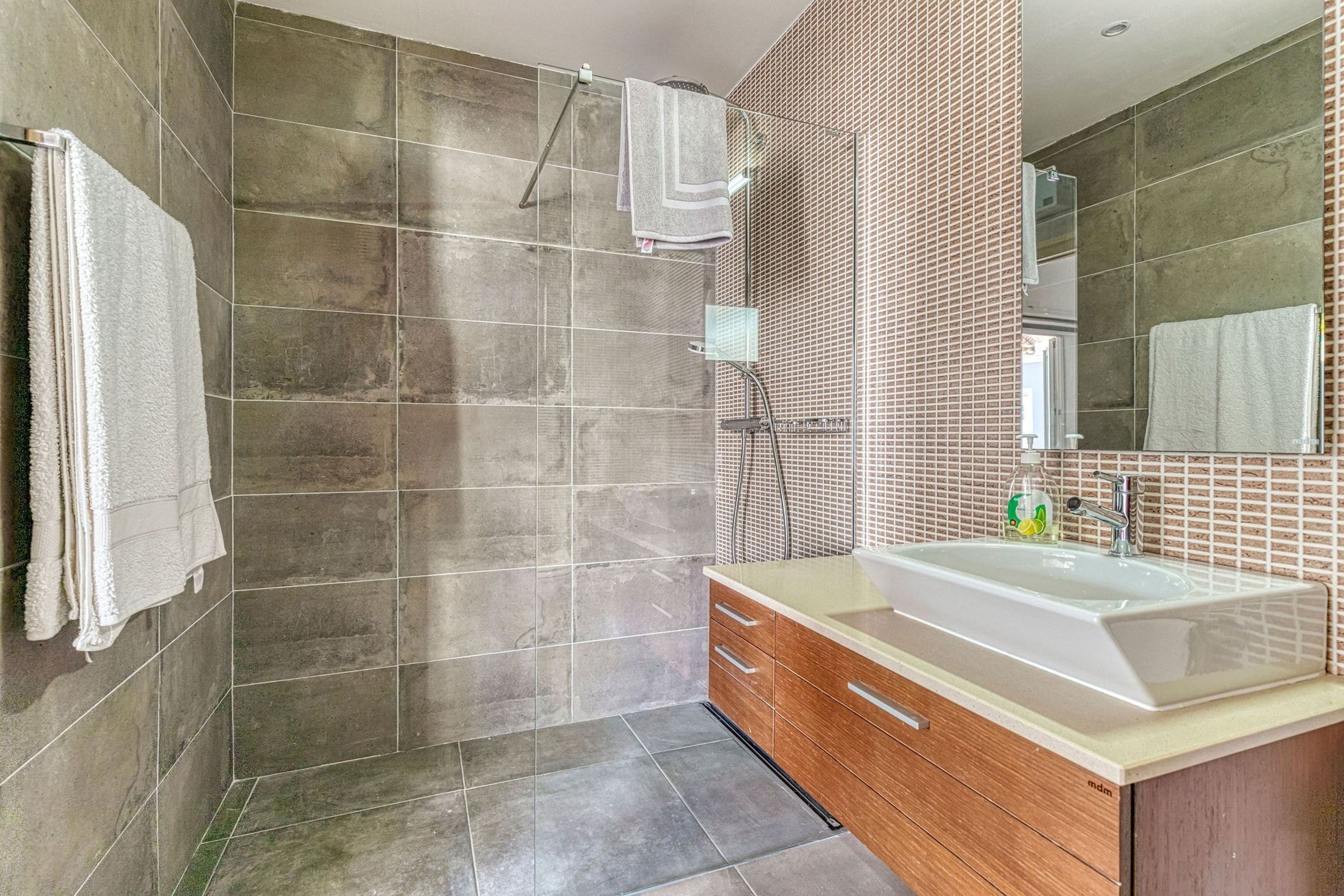 Een moderne badkamer met een ruime douche, een wastafel en een spiegel.
