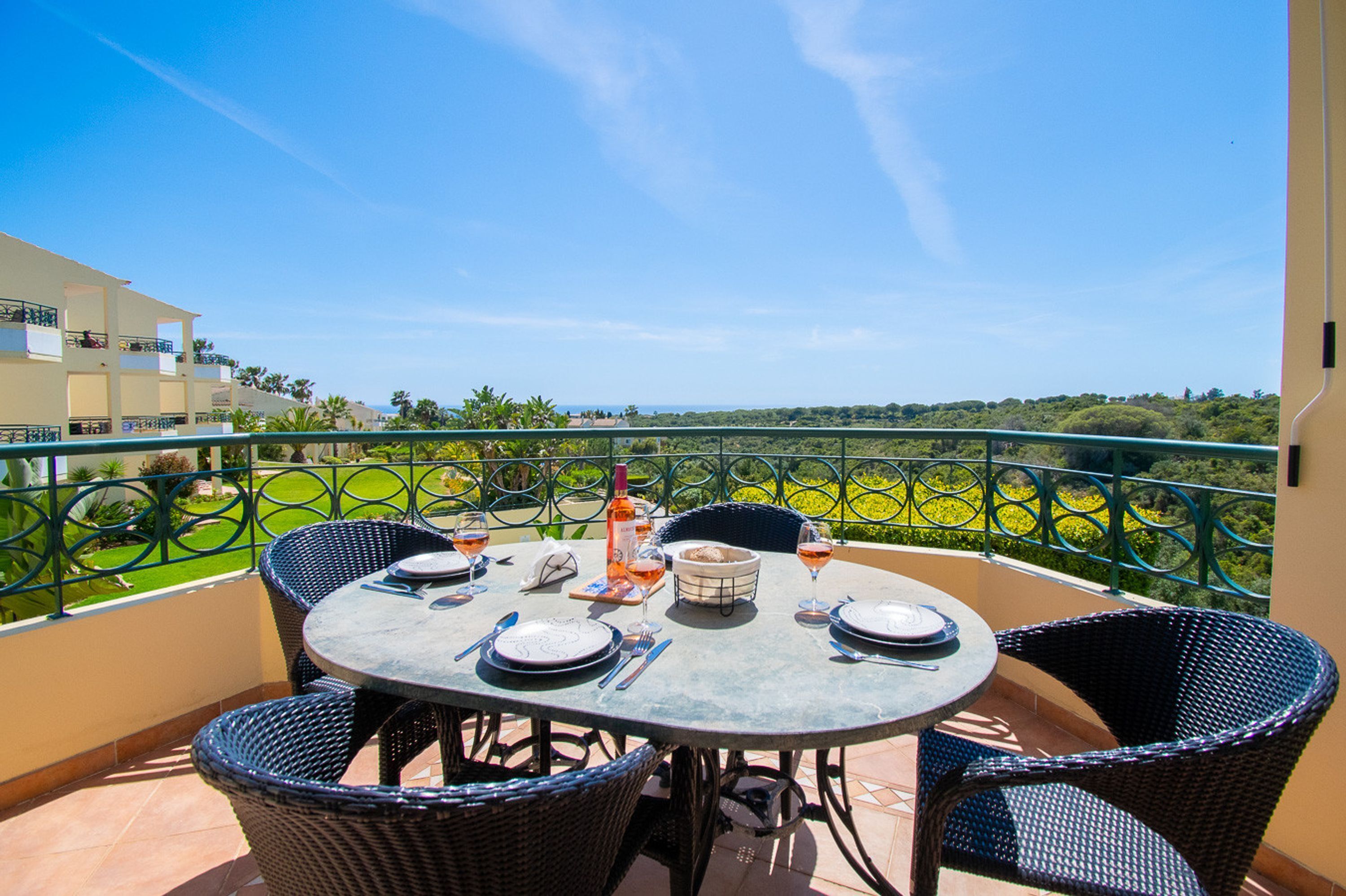 A round table with four chairs on a balcony, set for dining with plates, cutlery, and glasses.