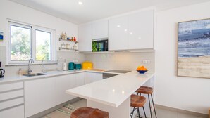 Une cuisine moderne avec des meubles blancs, un îlot central doté de tabourets, une fenêtre et un tableau accroché au mur.