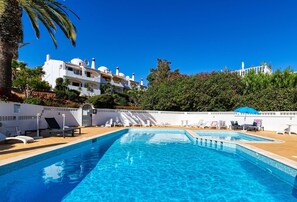 Ein Swimmingpool mit Liegestühlen und Sonnenschirmen, umgeben von einer weißen Mauer und Palmen.