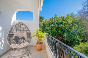 Ein Balkon mit einer Hängematte, einem Blumentopf und Blick auf Grünflächen.