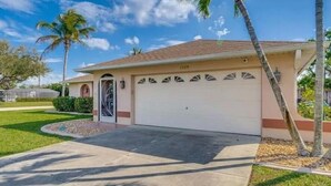 A single-story house with a garage, a front door, and a small front yard with a palm tree. - Relax at Cape Palm Oasis (Cape Coral)