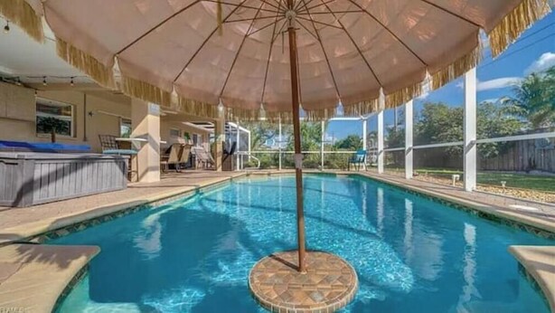A swimming pool with a central pole, surrounded by a covered area with a thatched roof. - Relax at Cape Palm Oasis (Cape Coral)