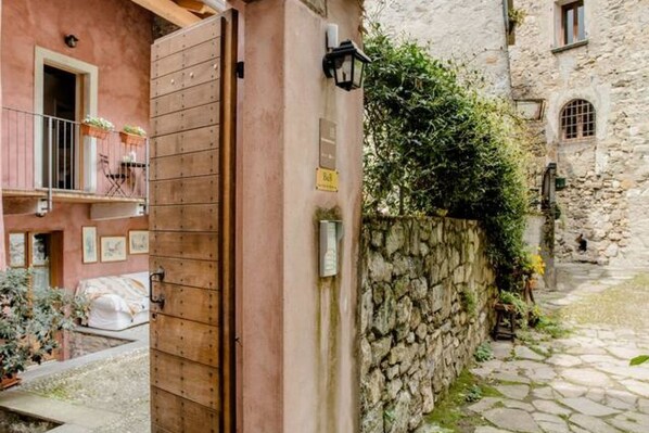 Une ruelle étroite, pavée de pierres, bordée d’un côté par un bâtiment rustique et de l’autre par une porte en bois.