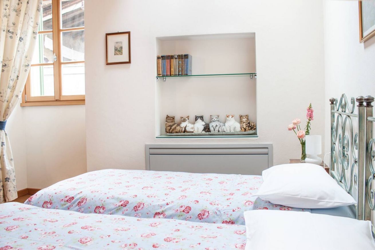Une chambre avec deux lits, une bibliothèque remplie de livres, un tableau encadré et une étagère décorative ornée de figurines.