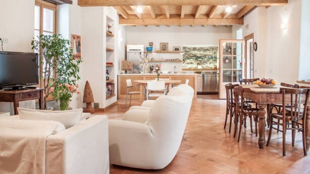 Un amplio espacio habitable con un sofá, una mesa de comedor con sillas, una cocina al fondo y un televisor sobre un mueble.