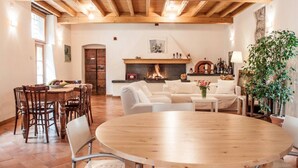 Una sala de estar amplia con chimenea, vigas de madera, un comedor con mesa redonda y un rincón de descanso acogedor.