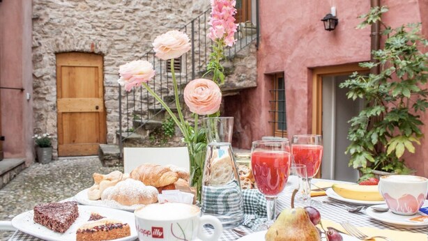 Disposición para comer al aire libre con pasteles, una taza de café y un bol de fruta.