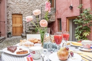 Disposición para comer al aire libre con pasteles, una taza de café y un bol de fruta.