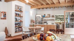 Un comedor con una mesa y sillas de madera, un frutero y una zona de cocina con estantes y electrodomésticos.