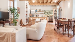 Amplia sala de estar con televisor, asientos cómodos, una mesa de comedor y una cocina al fondo.
