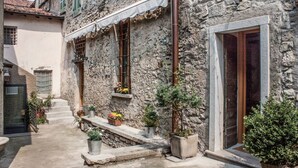 Un edificio de piedra con puerta y ventanas de madera, un pequeño espacio al aire libre con macetas y una escalera de piedra que lleva a la entrada.