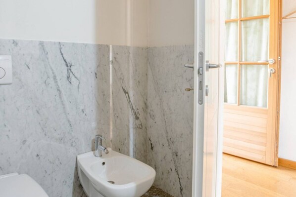 Un baño con pared de mármol, un bidé y una puerta de madera.