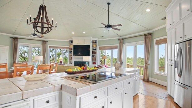 A spacious kitchen with a large island, white cabinetry, and a built-in TV. - Paradise Found | Ocean & Marsh Views (Edisto Island)