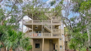 A two-story building with a balcony on the upper floor, surrounded by trees. - Paradise Found | Ocean & Marsh Views (Edisto Island)