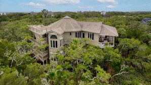 A large, multi-story house surrounded by dense greenery, with a prominent balcony and multiple windows. - Paradise Found | Ocean & Marsh Views (Edisto Island)