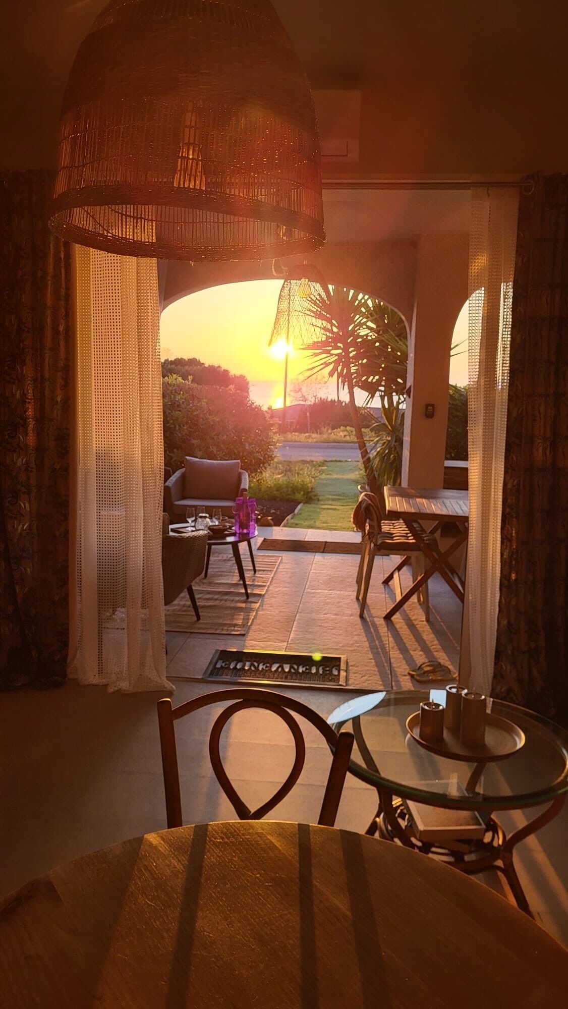 A room with a view of a sunset, a dining area with a table and chairs, and a sofa.