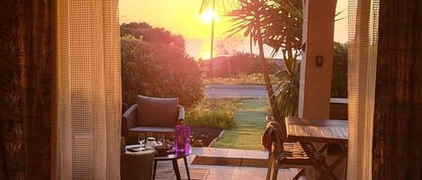 A room with a view of a sunset, a dining area with a table and chairs, and a sofa.
