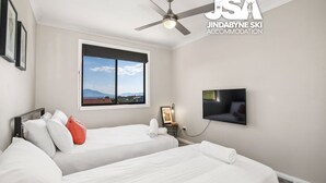 Une chambre d’hôtel avec deux lits, un ventilateur de plafond, une télévision et une fenêtre donnant sur la montagne.