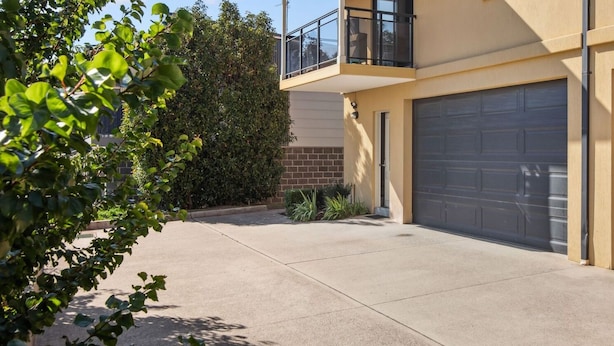 Un immeuble résidentiel doté de deux portes de garage, d’un balcon et d’une allée en béton.