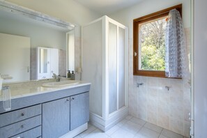 Un baño moderno con un espejo grande, dos lavamanos, una ducha y una ventana con cortina.