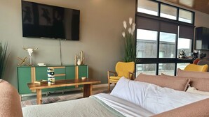 A modern living room with a green console table, a yellow armchair, a large flat-screen TV, and a view of the outdoors through large windows. - Cactus & Cabernet~Tesla Charger~Hot Tub~Waffle Bar (Quincy)