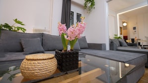 A modern living room with a glass coffee table, grey sofas, and a potted plant with pink flowers. - Ruby's Urban Residence Koukaki (Athens)