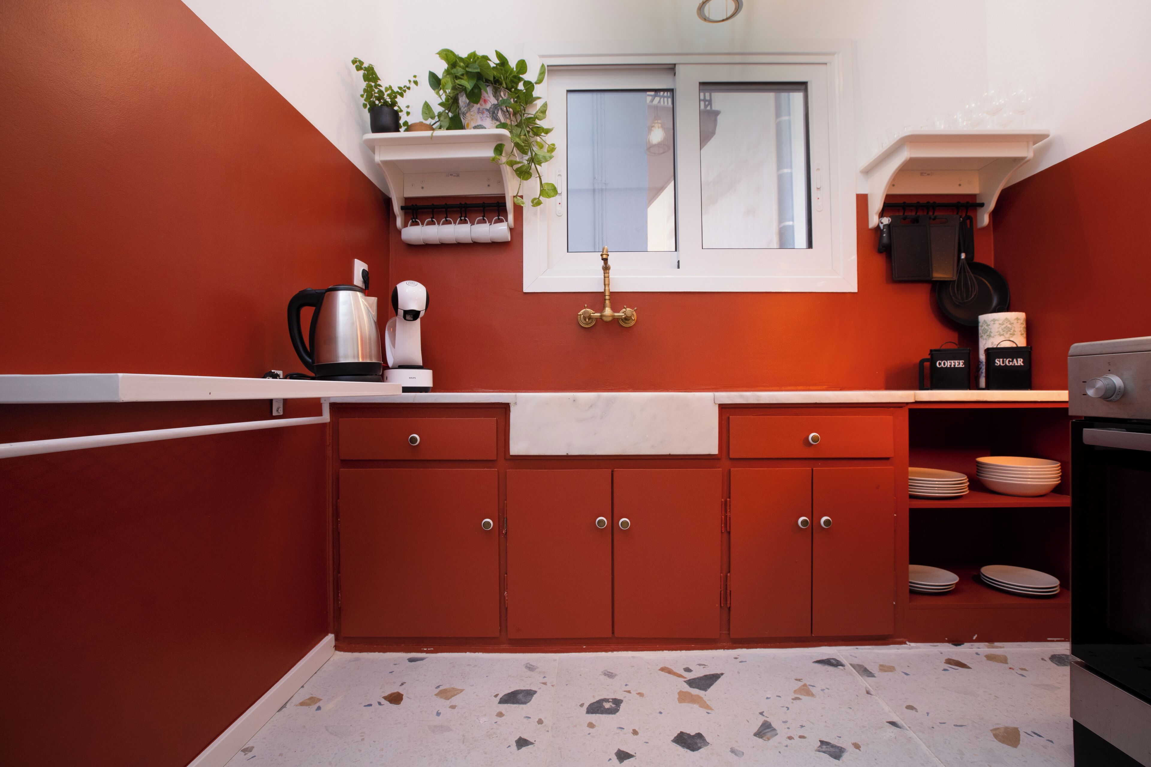 A compact kitchen with red cabinetry, a window, and a countertop with a kettle and coffee maker.
