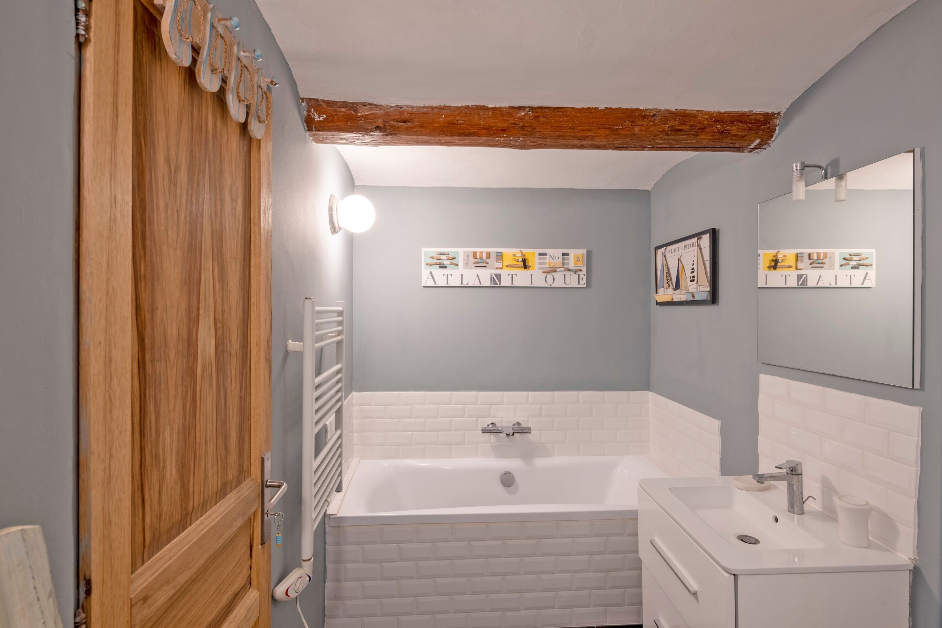 Un baño con puerta de madera, bañera blanca, lavabo y espejo.