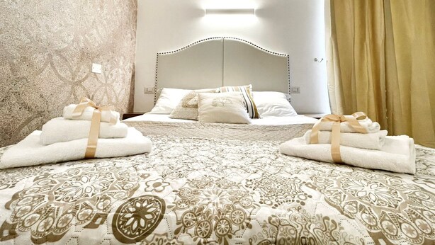 A hotel room with a bed, two sets of towels, a patterned bedspread, and a plain wall. - BARI ROOMS Abate Gimma (Bari)