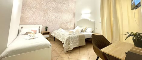 A hotel room with two beds, a small table, a chair, a TV, and a potted plant.