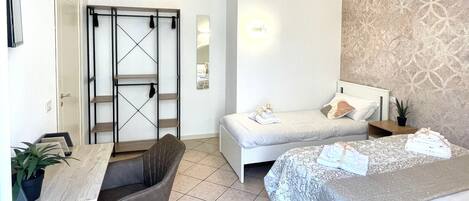 A bedroom with two beds, a desk, and a chair. There is a wardrobe with a mirror and a door.