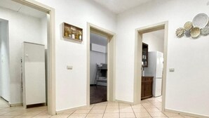 A hallway with white walls, a tiled floor, and a door leading to a kitchen area with cabinets and a refrigerator. - BARI ROOMS Abate Gimma (Bari)