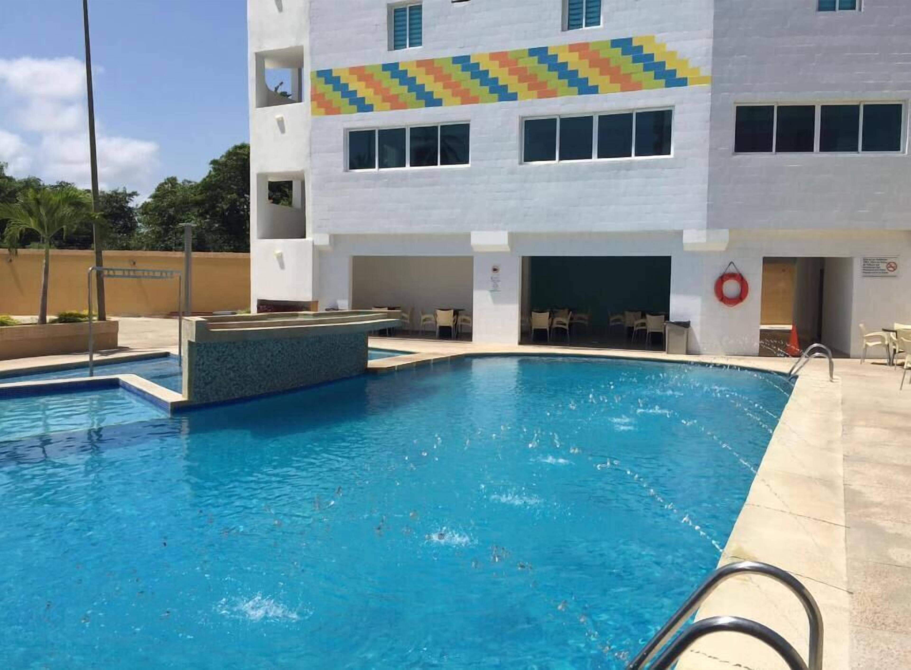 A swimming pool with a white building in the background, a lifebuoy, and a no swimming sign.