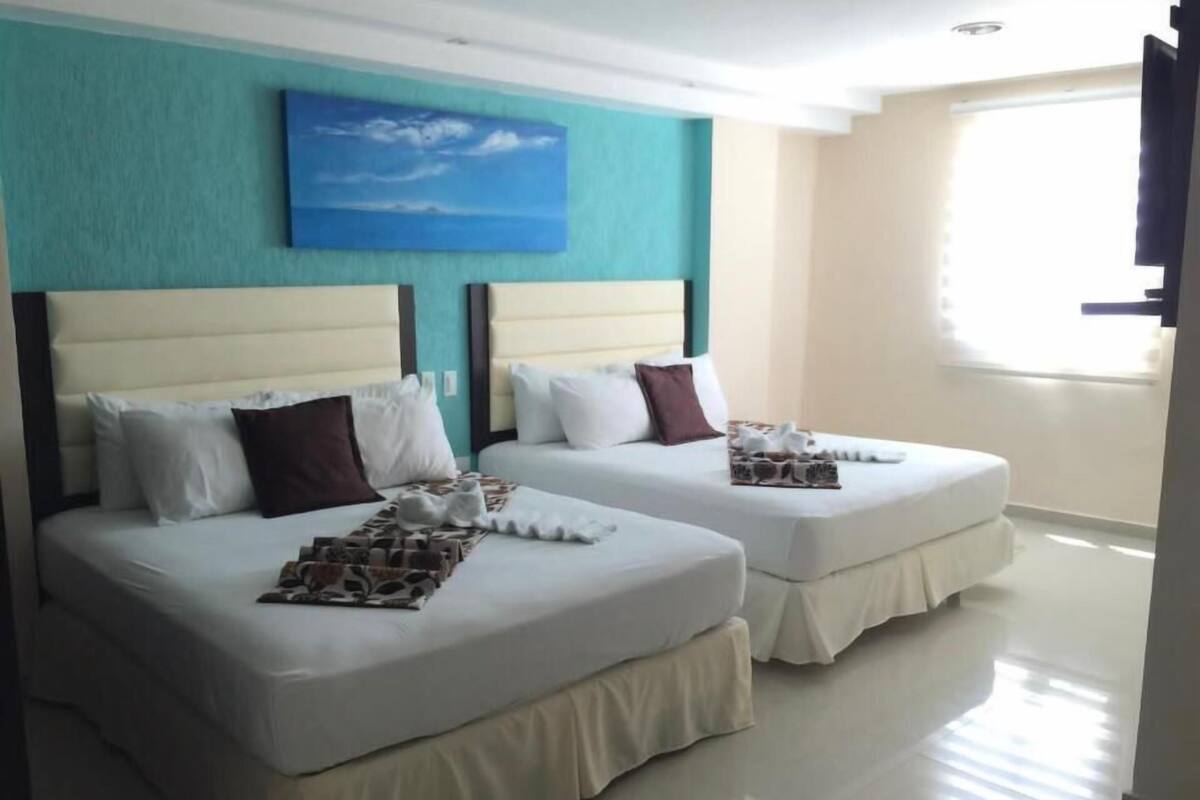 Twee bedden met queensize, wit bedlinnen, een muur in teal-kleur en een schilderij van een blauwe lucht.